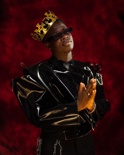 Free Stylish portrait of a man wearing a crown and sunglasses against a red backdrop. Stock Photo
