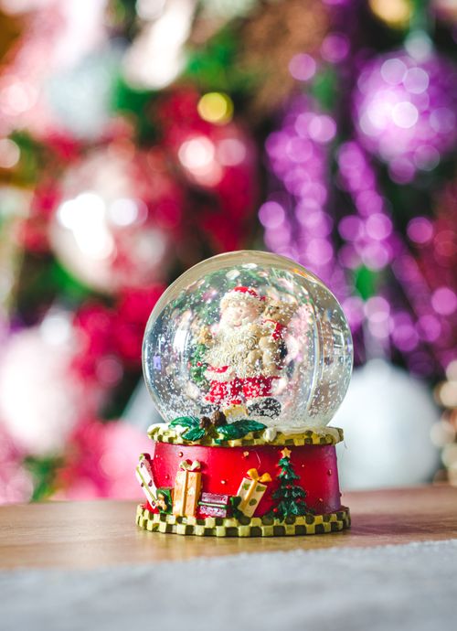 Free Close-up of a Santa Claus snow globe on a wooden surface with a vibrant bokeh Christmas background. Stock Photo