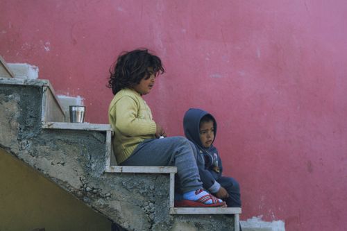 Free Two children sitting on outdoor stairs against a vibrant pink wall, in casual clothing. Stock Photo