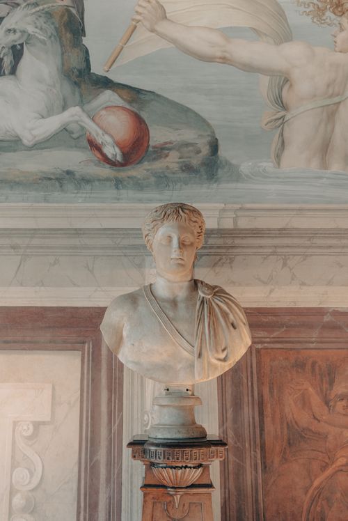 Free Elegant marble bust displayed against a Renaissance-style mural in Florence, Italy. Stock Photo
