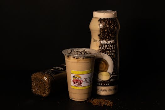 A close-up of coffee products including a flavor creamer and instant coffee jar against a black background.