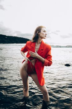 Stylish woman in a red blazer standing in the ocean, posing elegantly.