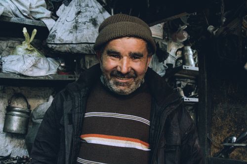 Free Portrait of a smiling middle-aged man wearing a beanie in a cluttered workshop, expressing warmth. Stock Photo
