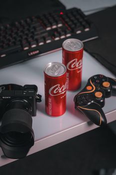 Close-up of Coca-Cola cans with camera and game controllers on a desk.