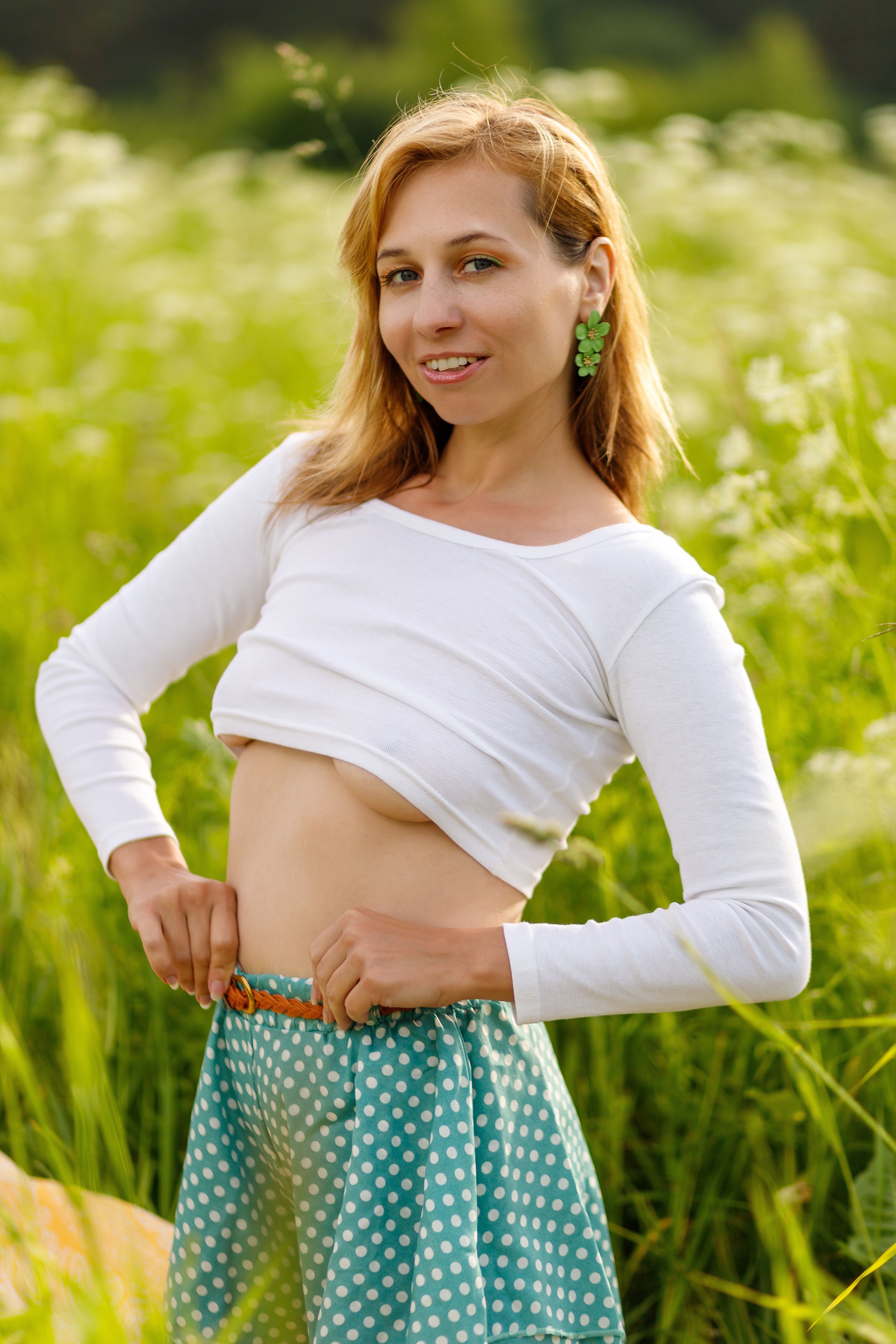 Styled portrait of a woman in a polka dot skirt posing confidently in a sunny meadow.