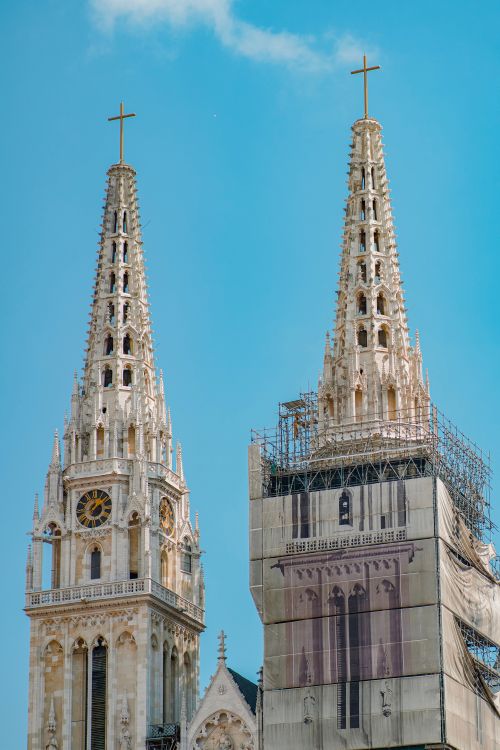 Free Two Gothic cathedral towers with crosses, one under renovation against a blue sky. Stock Photo