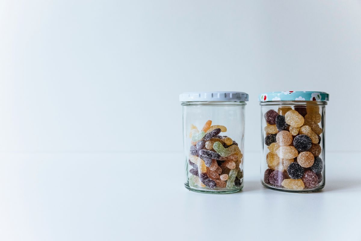 Colorful gummies and sugared candies in glass jars on a white surface. Minimalist style.
