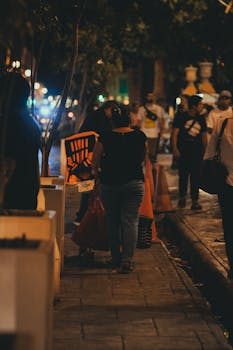 A bustling nighttime city street filled with people walking under street lights.