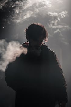 Silhouette of a man smoking in a foggy atmosphere with dramatic lighting.