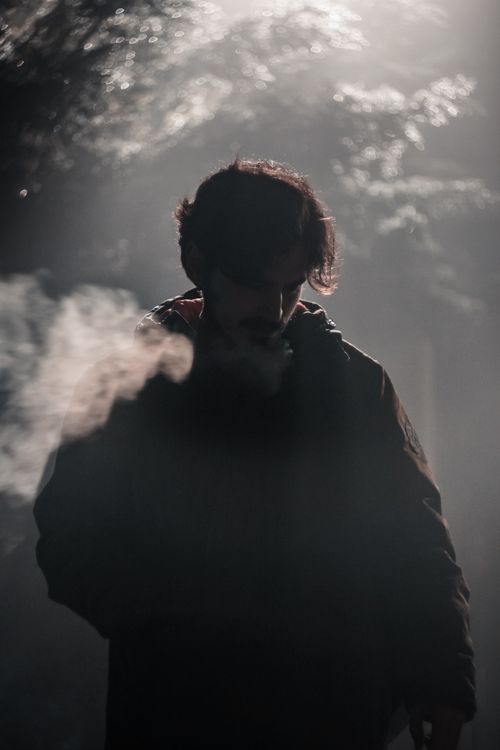 Free Silhouette of a man smoking in a foggy atmosphere with dramatic lighting. Stock Photo