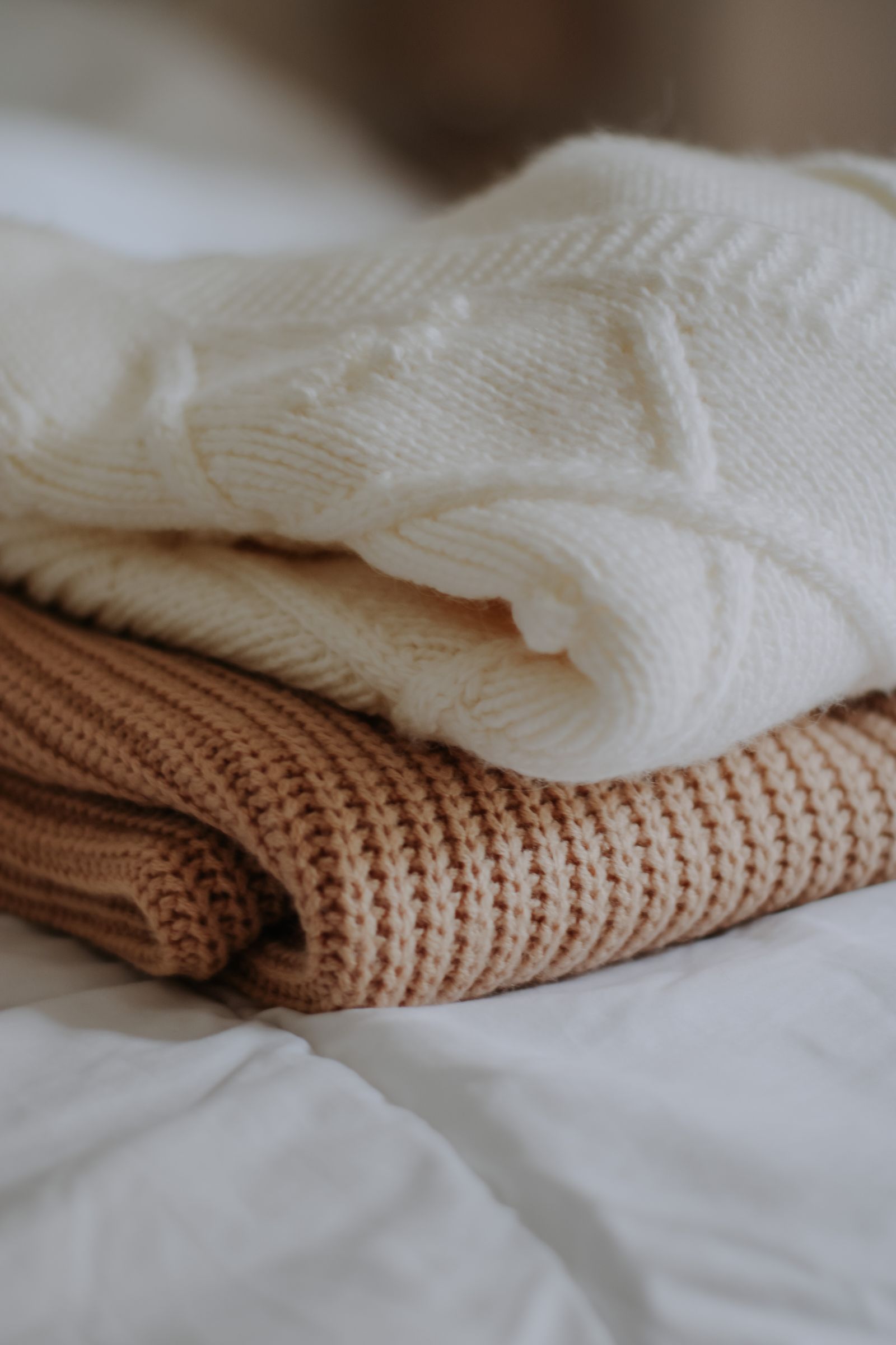 Folded wool jumpers stacked in a quiet room, daylight from one side