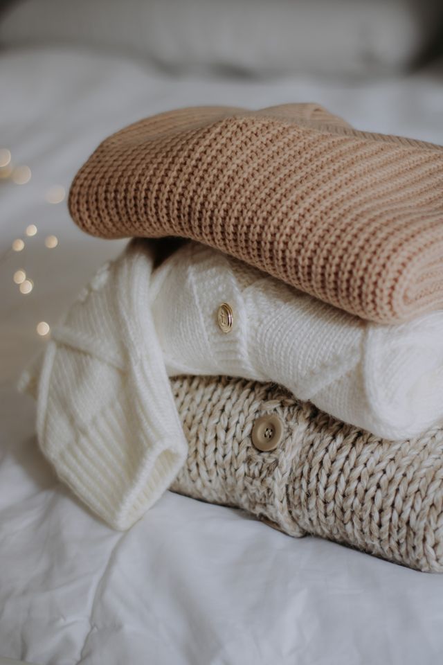 Stacked pile of knitted sweaters in neutral tones, photo by Nati on Pexels