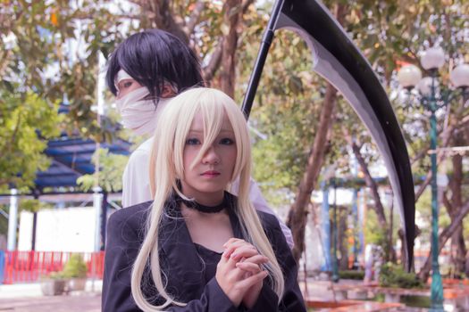 Two cosplayers pose in a park setting, showcasing intricate costumes and props.