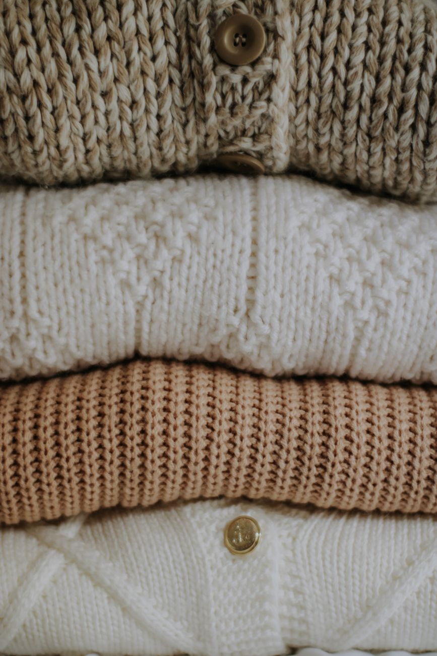 Stacked neutral knit sweaters with buttons, highlighting texture and warmth.