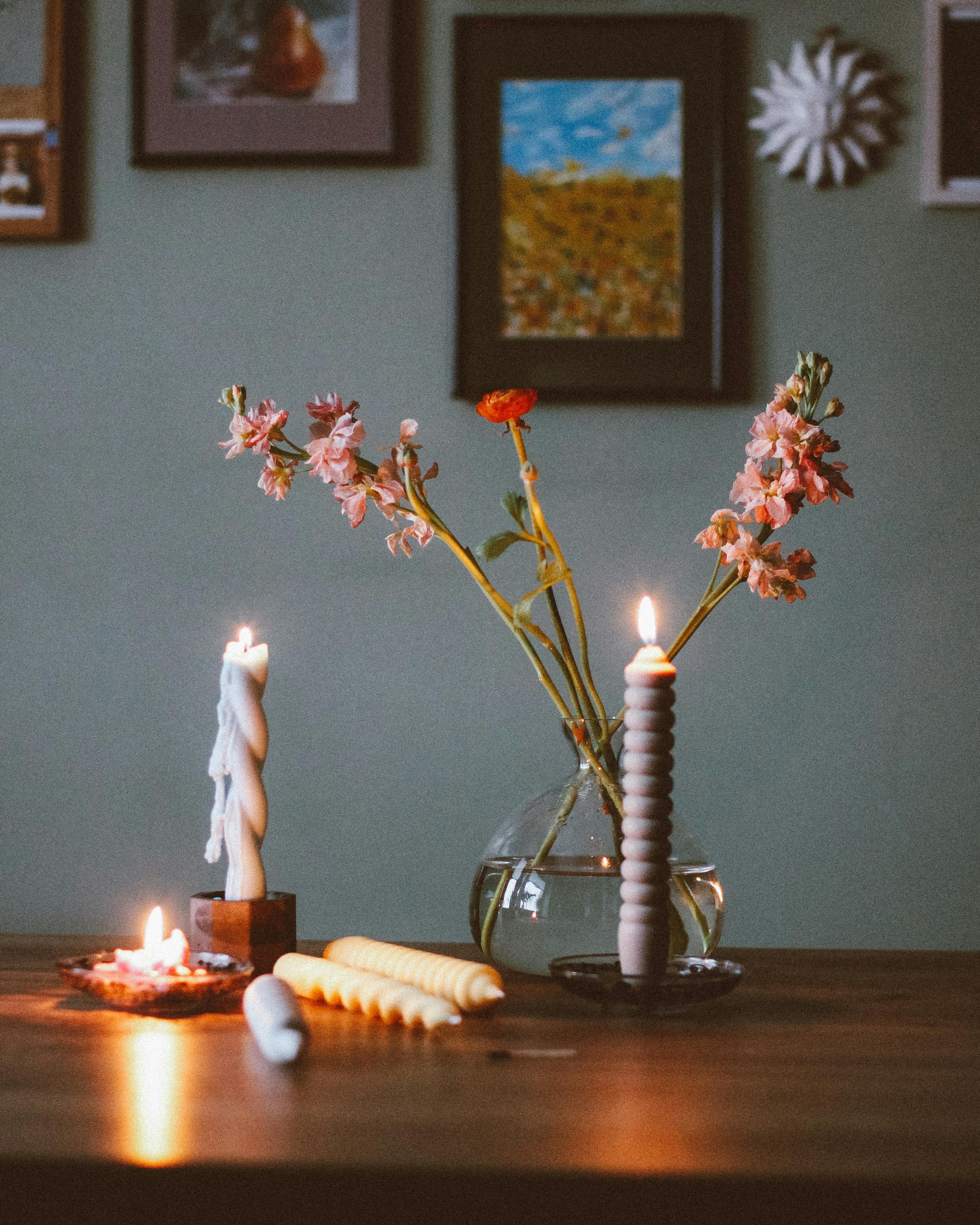 A warm, cozy still life featuring candles, flowers, and home decor on a wooden table.
