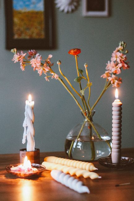 A cozy still life featuring flowers in a vase with candles on a wooden table.