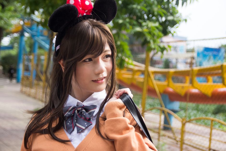 Young woman in a Minnie Mouse headband smiling outdoors in a theme park.