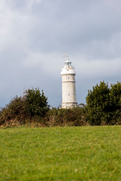 Free Lighthouse amidst green fields under a dramatic sky in Santander, Spain. Stock Photo