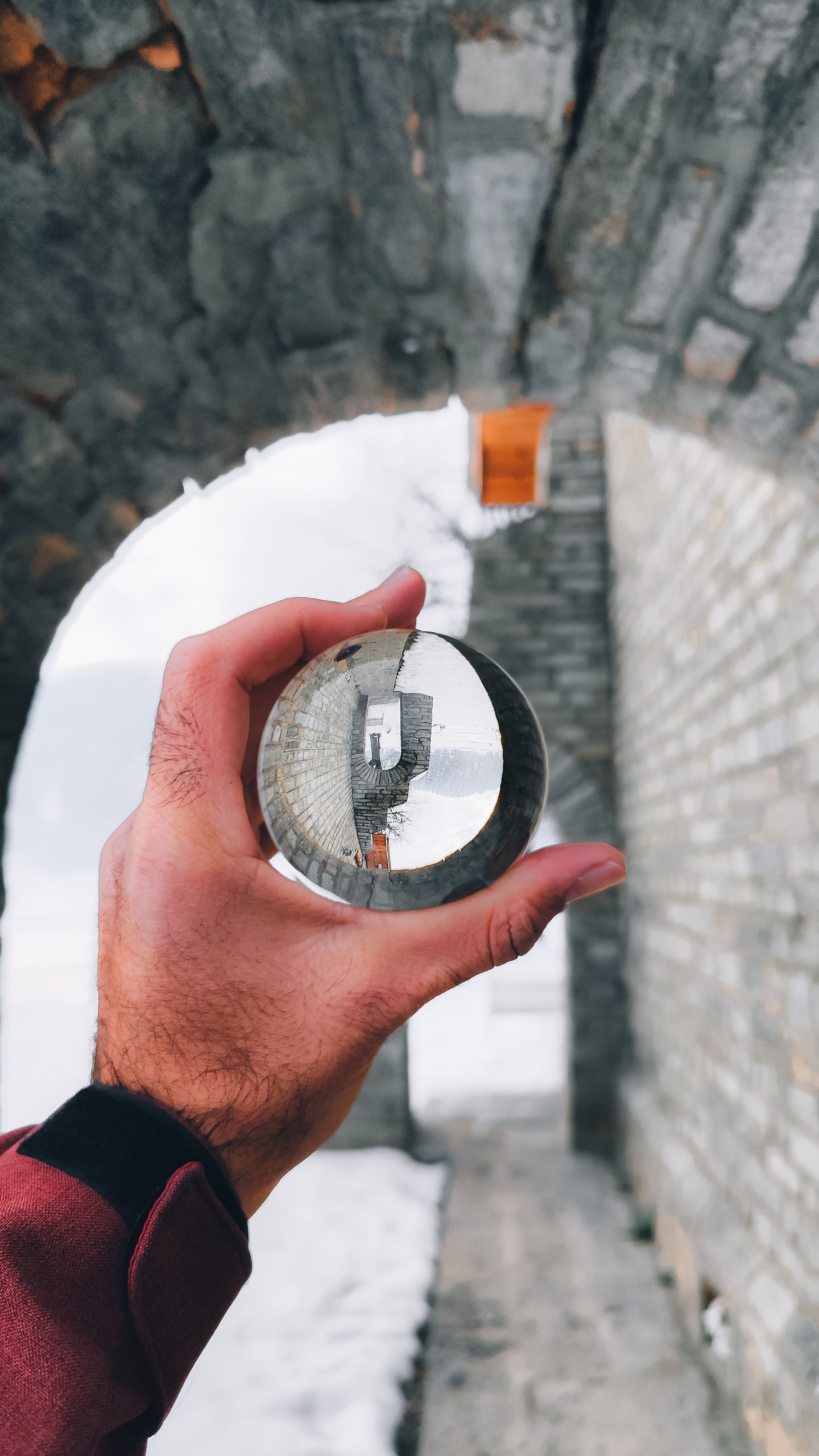 Hand holding a crystal ball reflecting an archway and snowy scene, creating an upside-down illusion.