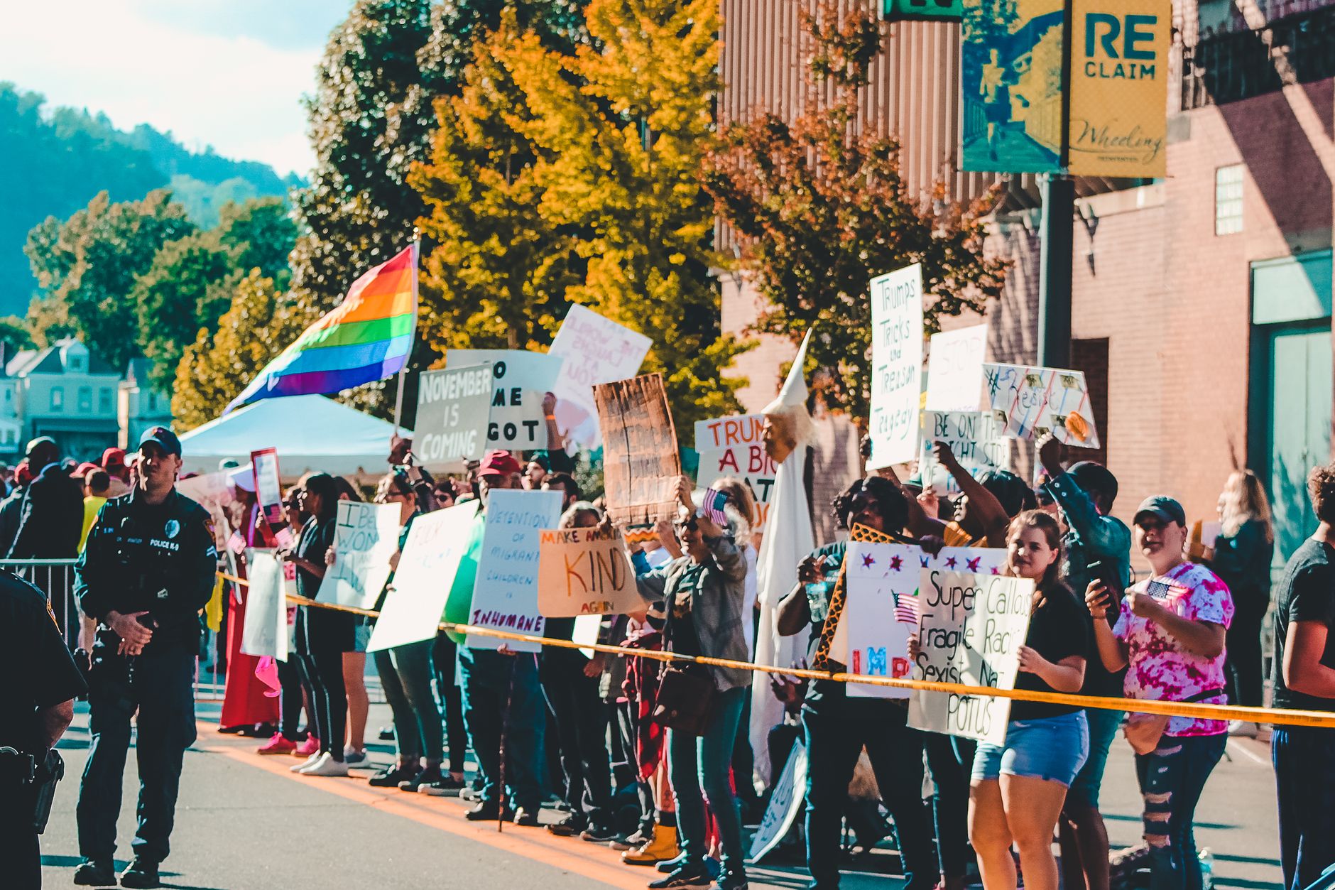 Protesters in Wheeling, WV, hold signs and flags in a diverse, peaceful demonstration on a sunny day.