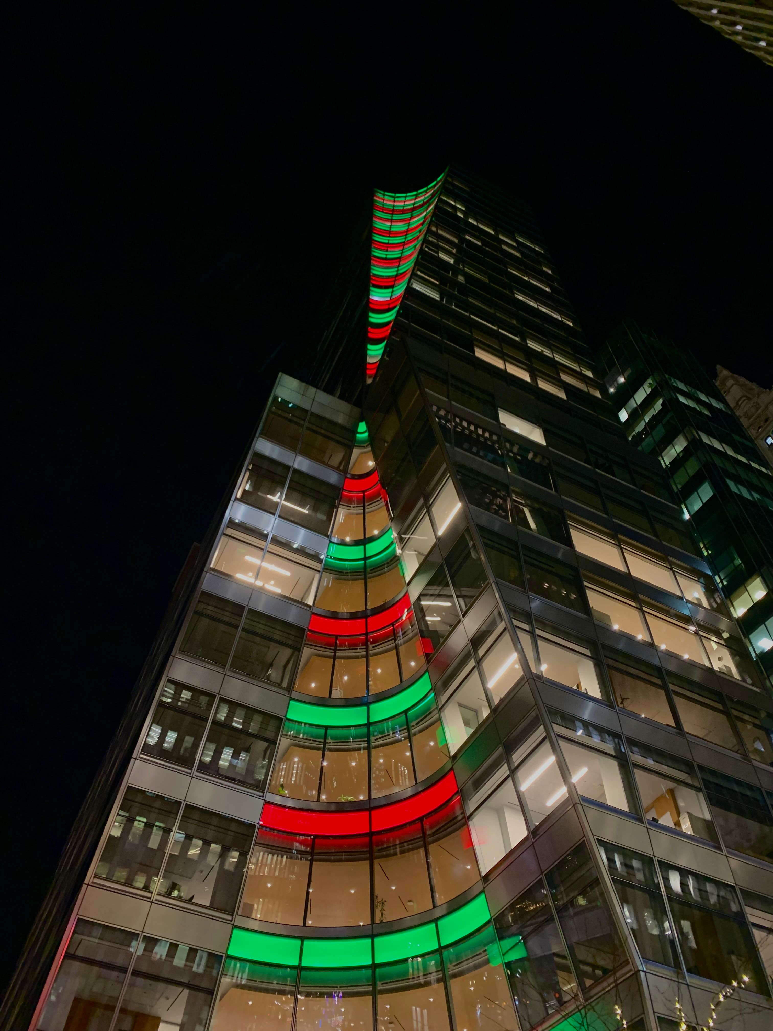 A modern skyscraper illuminated with colorful festive lights during nighttime in an urban setting.
