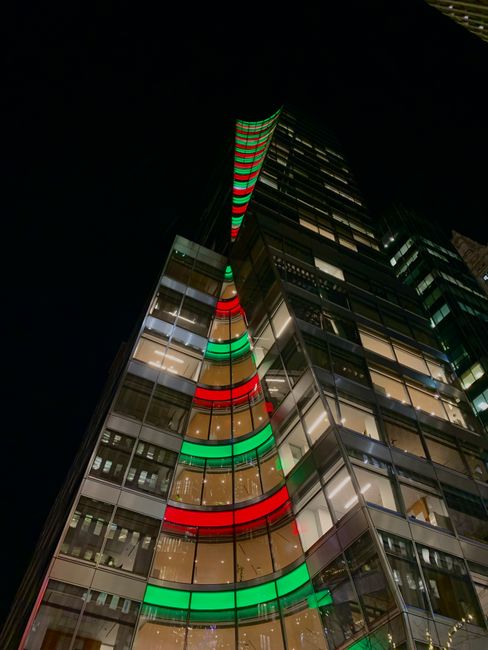 A modern skyscraper illuminated with colorful festive lights during nighttime in an urban setting.