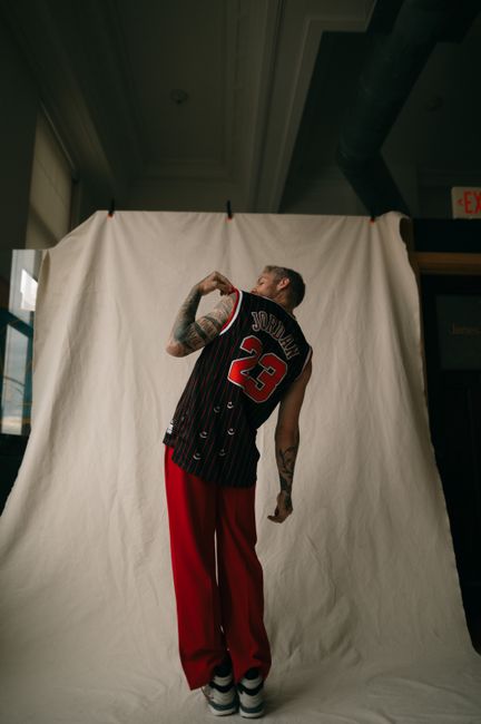 Back view of a man in a Jordan jersey with tattoos, standing indoors.