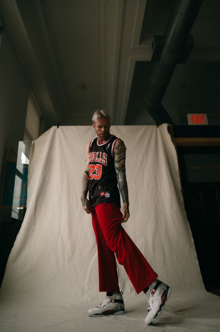 Fashionable man with tattoos posing in basketball jersey and red pants indoors.