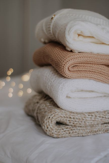 Aesthetic stack of soft knitted sweaters in neutral tones, cozy atmosphere.