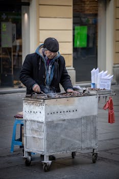 An elderly vendor cooking chestnuts on a street cart, captured in an urban setting.