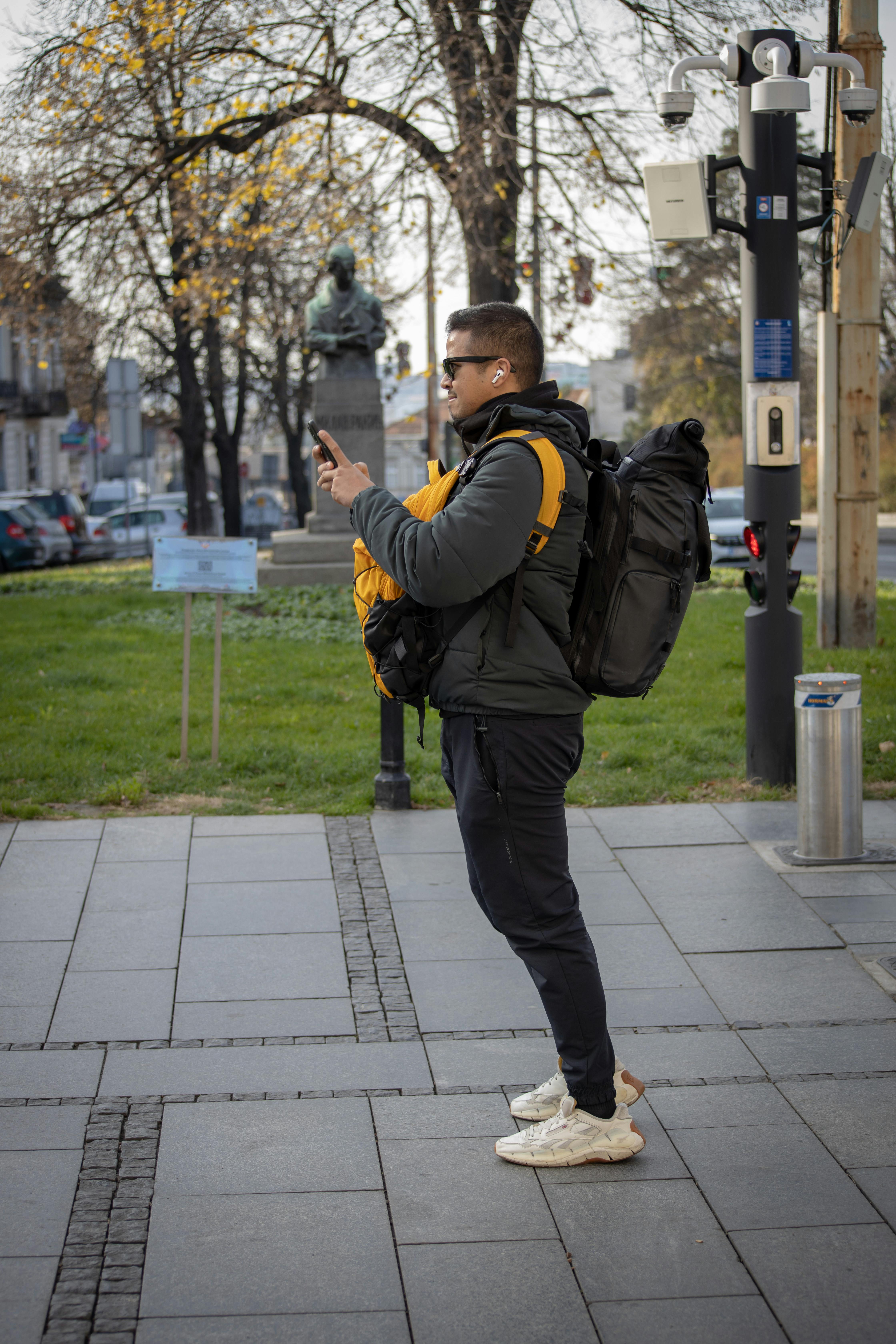 a man in a puffer jacket carrying backpacks while using his smartphone