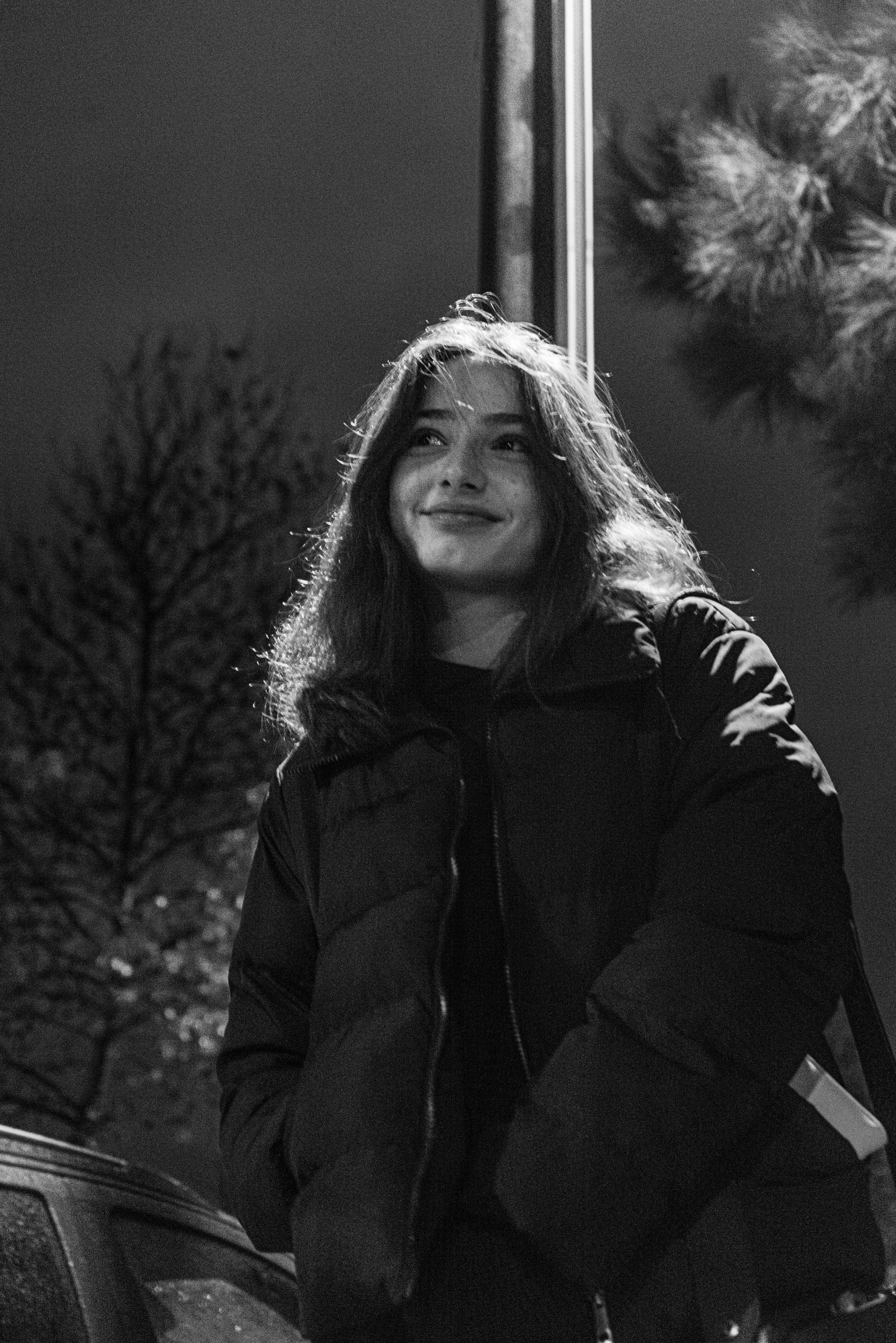 A smiling woman in a jacket captured outdoors at night in black and white.