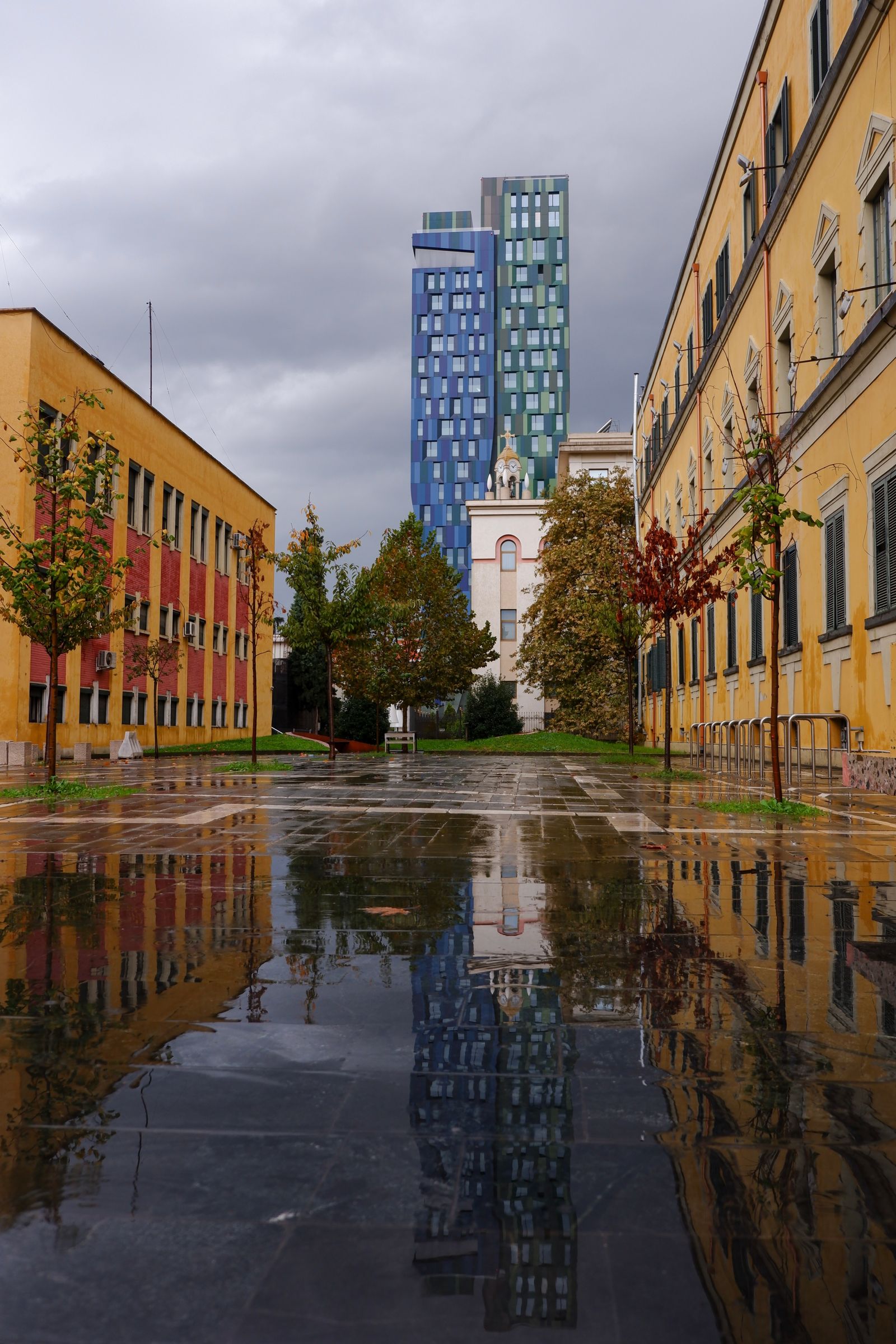 Tall buildings reflected in a rain puddle on a pavement in Tirana, Albania