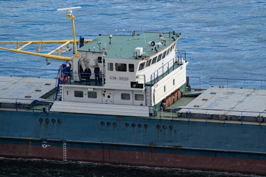Close-up view of cargo ship with crew at the helm, navigating open blue waters.