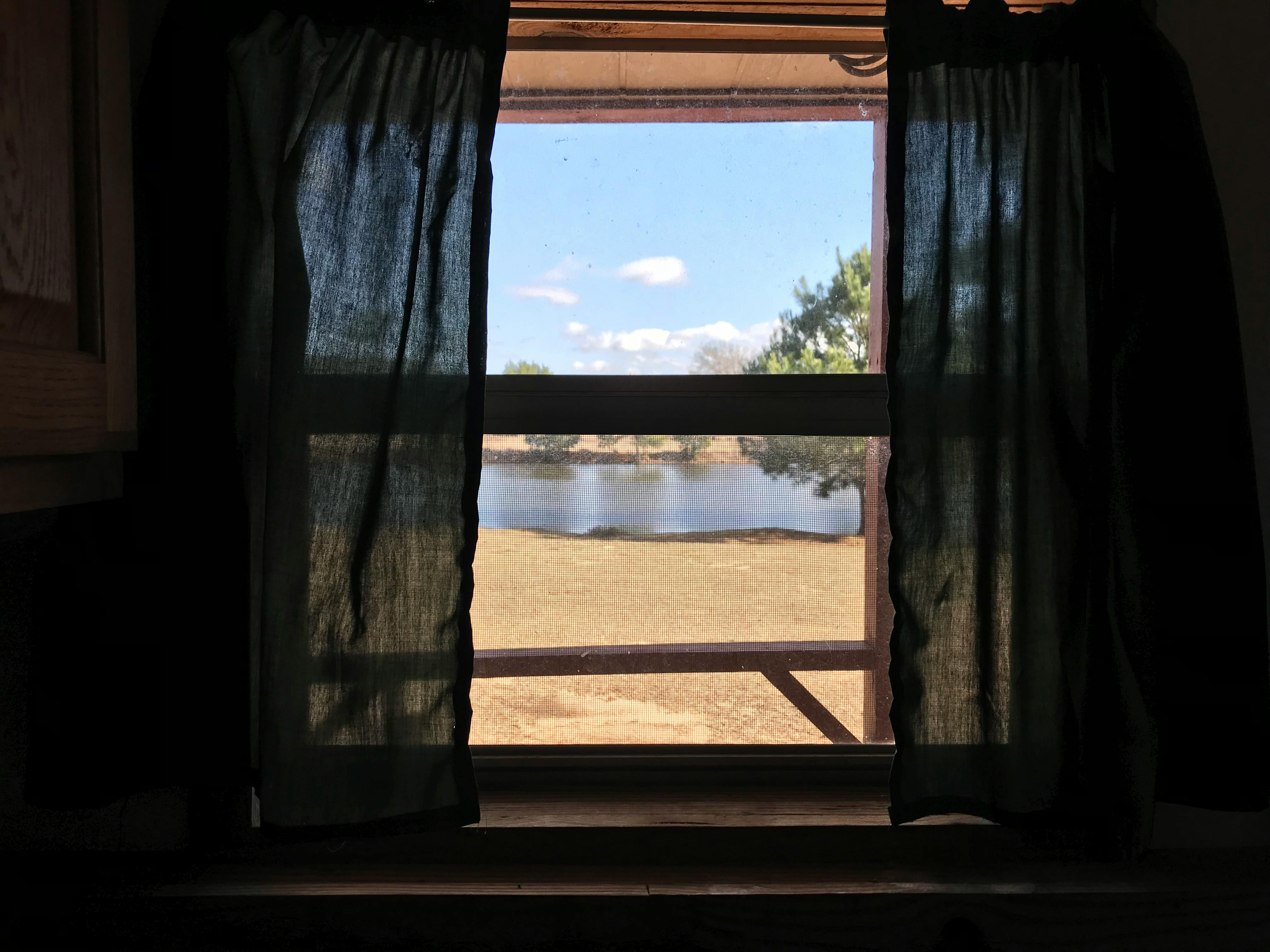 Peaceful lake view framed by dark curtains on a sunny day, providing a tranquil indoor setting.