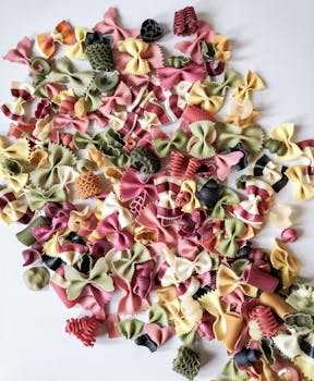 Vibrant mixed bow tie pasta scattered on a white surface showcasing various shapes and colors.