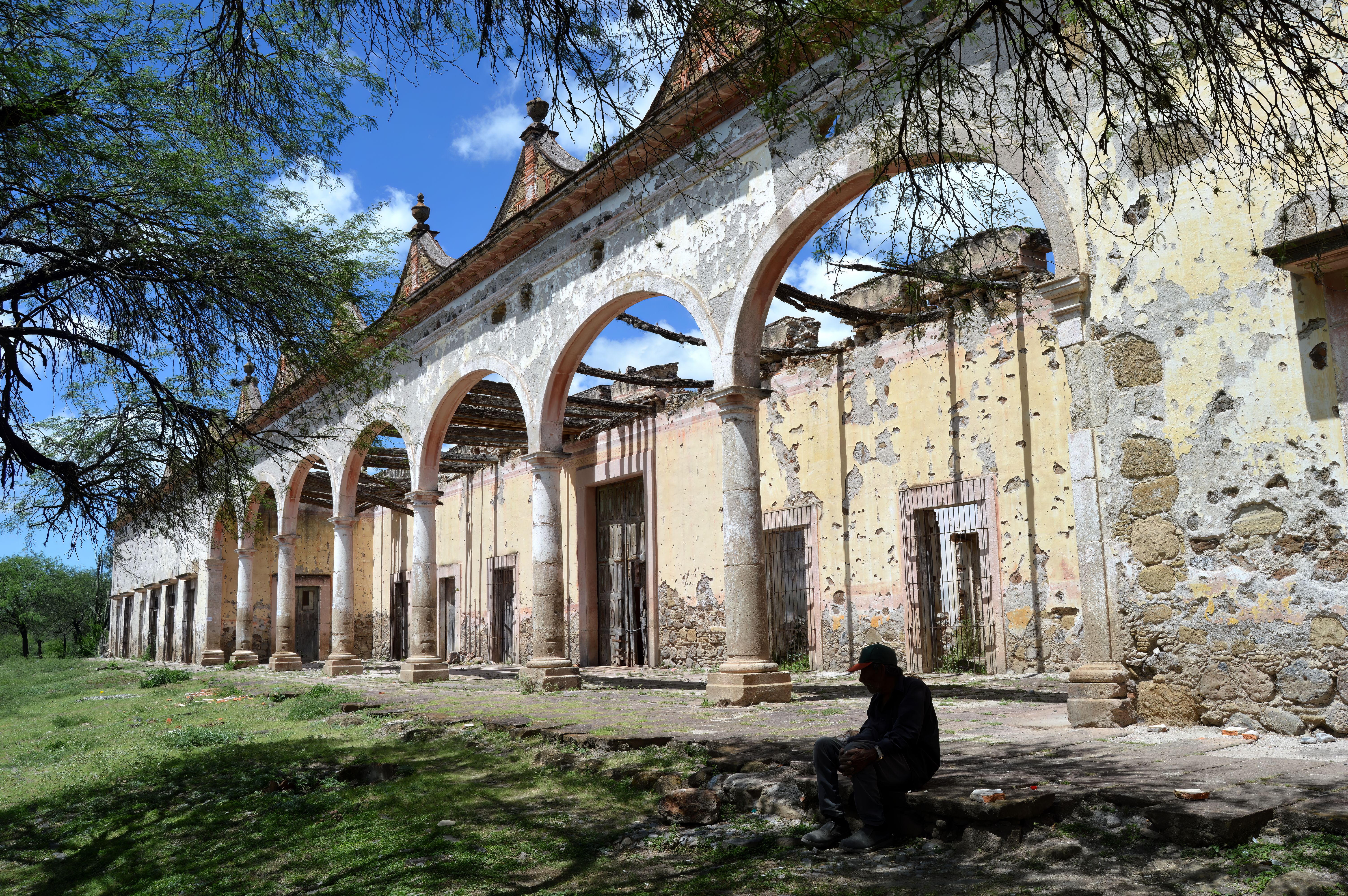 A man sits by an old archway facade under a clear blue sky, showcasing historic architecture.