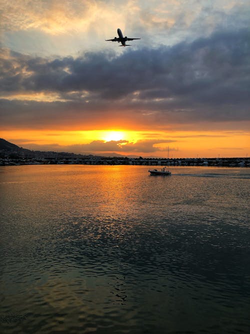 Airplane in the Sky and Boat on Sea During Sunset