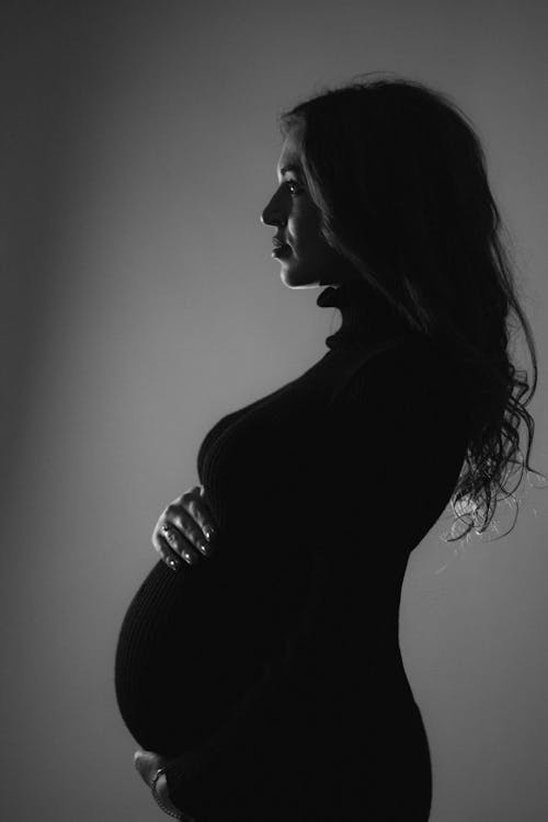 Grayscale Photography of a Woman Touching Her Baby Bump while Looking Afar