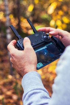 Close-up of hands holding a drone controller outdoors in a fall setting.