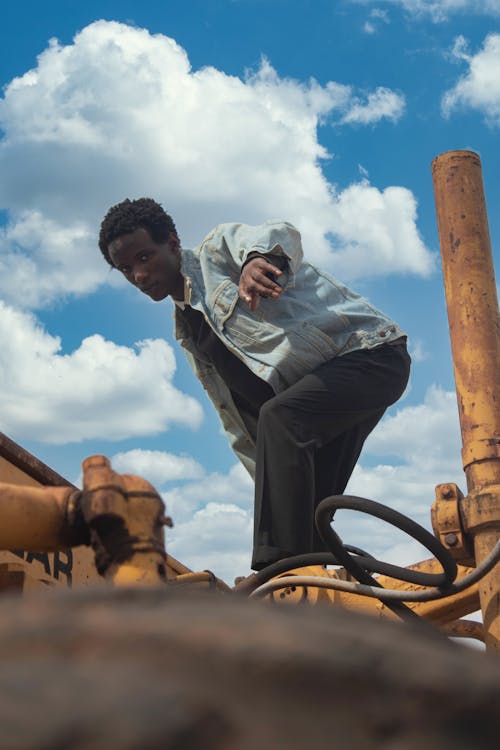 A Man in Denim Jacket Standing Near Metal Pipes while Posing at the Camera 