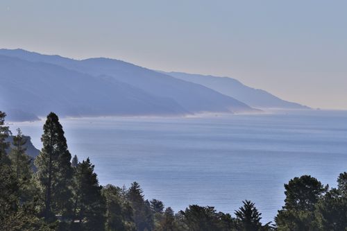 Free Serene view of a misty coastline with mountains and lush forests along a calm sea. Stock Photo
