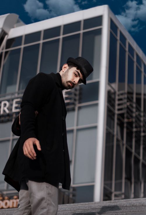 Free A fashionable man poses with confidence in an urban setting, wearing a stylish hat. Stock Photo