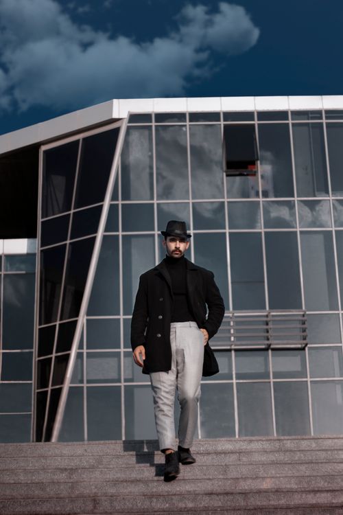Free Man in fashionable attire walks confidently near modern glass building exterior. Stock Photo