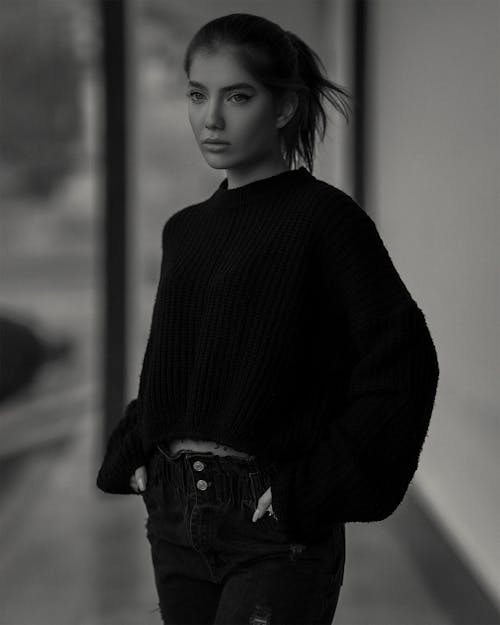Woman in Sweater With Hands in Her Pockets in Grayscale Photography 