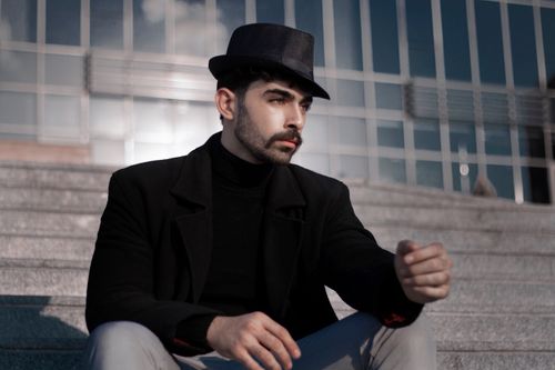 Free Fashionable man in a black hat sits on stairs in an urban setting. Stock Photo