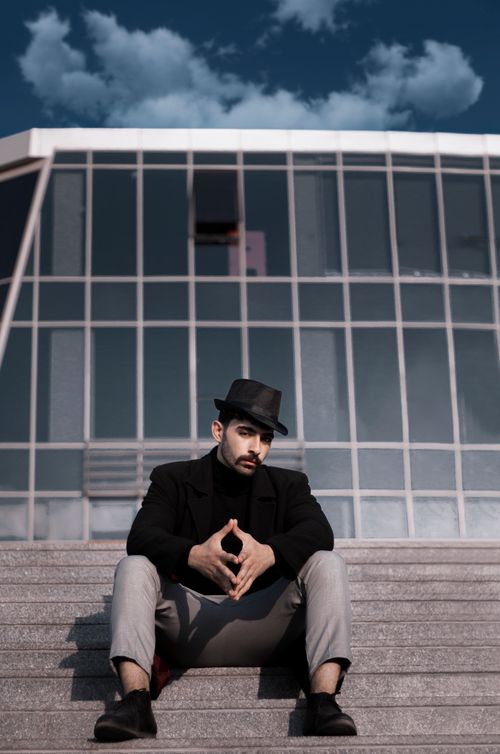 Free Confident man in hat posing on concrete steps against modern architecture. Stock Photo