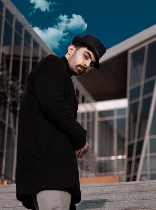 Free A fashionable man wearing a black coat and top hat outside a modern building. Stock Photo