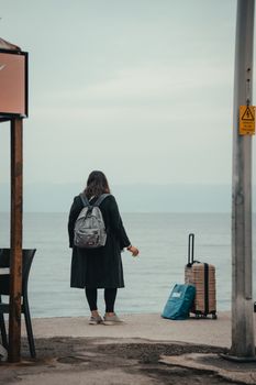 Woman with backpack looking at the sea beside suitcase, ready for adventure.