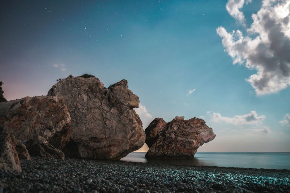 A stunning night view of rock formations on a beach with a calm sea under a starry sky.